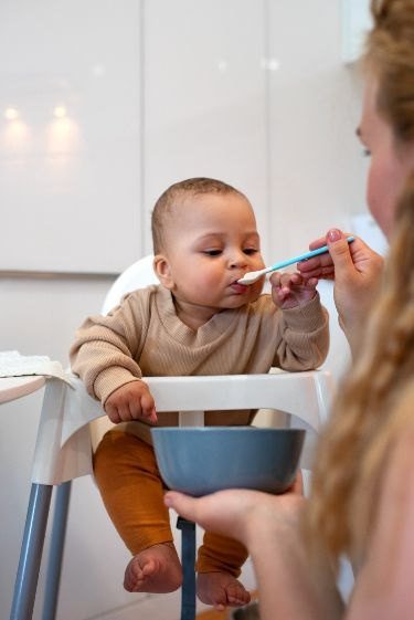 Bebê na cadeirinha provando comida na colher
